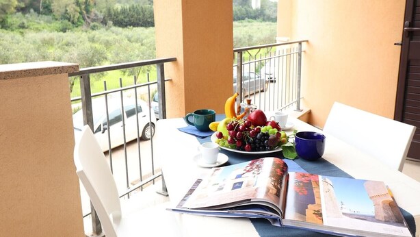 A balcony with a table set for breakfast, a magazine, and a view of greenery and a bridge. - Holiday Apartment “Claudia” with Air Conditioning and Balcony (otranto)