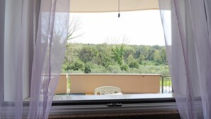 A balcony with a white chair, sheer curtains, and a view of a forested hillside. - Holiday Apartment “Claudia” with Air Conditioning and Balcony (otranto)