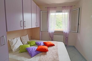 A bedroom with a bed, a window with curtains, and a radiator.