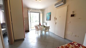 A room with a bed, a dining table with chairs, a painting on the wall, and an air conditioning unit. - Holiday Apartment “Claudia” with Air Conditioning and Balcony (otranto)
