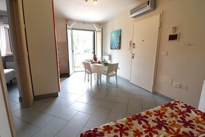 A room with a bed, a dining table with chairs, a painting on the wall, and an air conditioning unit.