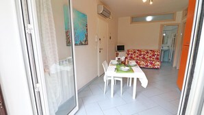A dining area with a table set for two, a sofa, and a kitchen area in the background. - Holiday Apartment “Claudia” with Air Conditioning and Balcony (otranto)