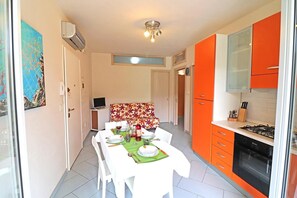 A dining area with a table set for four, a kitchen with orange cabinets, and a ceiling light fixture.