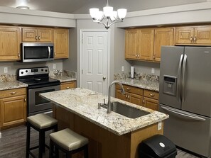 A modern kitchen with wooden cabinets, stainless steel appliances, a granite countertop, and a central island with stools.