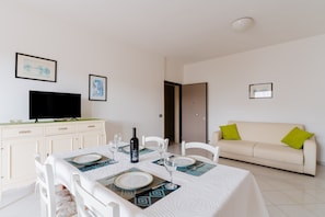A dining area with a table set for four, a sofa, and a television in a room with white walls and a door.