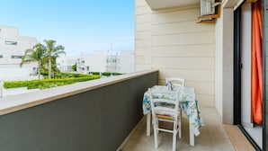 Ein Balkon mit Tisch und Stühlen, Blick auf Gebäude und eine Palme.