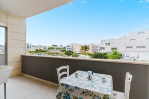 A balcony with a table and chairs, a view of buildings, and a clear sky.