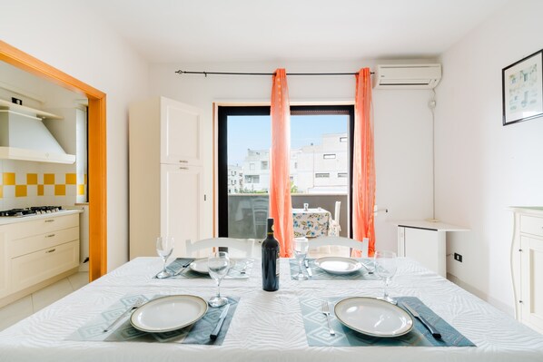 A dining area with a table set for two, a bottle, and a window with curtains.