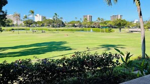 Ein Golfplatz mit blauem Himmel, Palmen und Gebäuden im Hintergrund.