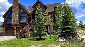 A log cabin with a stone chimney, large windows, and a stone staircase leading to the entrance. - Larkspur Luxury - Crested Butte (Crested Butte)