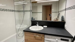Une salle de bain moderne dotée d’une douche à parois de verre, d’un lavabo avec un plan de travail noir et d’un lave-linge encastré.