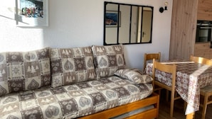 Une pièce chaleureuse avec un canapé à motifs, une table à manger recouverte d’une nappe à carreaux et un miroir au mur.