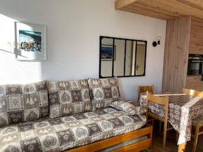 Een gezellige kamer met een gestreept bankje, een eettafel met geruit tafelkleed en een spiegel aan de muur.