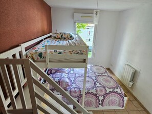 Une chambre avec deux lits superposés, une fenêtre donnant sur le paysage, un radiateur et une porte menant à l’extérieur.