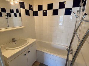 A bathroom with a white sink, mirror, and a bathtub with a showerhead. - Central Apartment in Biscarrosse with Pool and Terrace, Beach Nearby, Sleeps 4 (Biscarrosse)