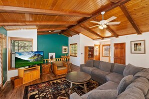 A living room with a large flat-screen TV, a grey sectional sofa, a round coffee table, and a wooden ceiling. - The Family Cabin by Destination Big Bear : Moonridge Chalet Close to Bear Mtn, Golf Course & Zoo! Spa! Pool Table! (Big Bear Lake)