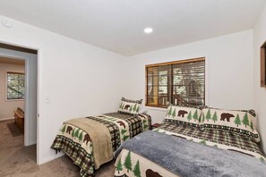 Ein Schlafzimmer mit zwei Betten, einem Fenster mit Jalousien, einer Tür zu einem anderen Raum und einer Bank in der Ecke.
