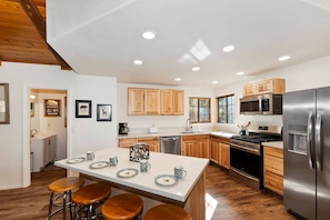 A modern kitchen with wooden cabinets, a stainless steel refrigerator, and a central island with stools.