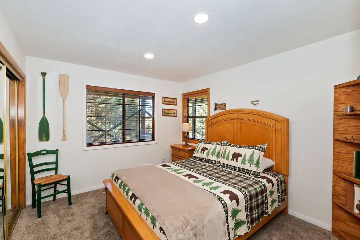 A bedroom with a wooden bed, a chair, a window with blinds, and a wall-mounted shelf.