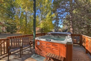 Ein Whirlpool auf einer Holzterrasse mit Holzzaun und Stühlen, umgeben von Bäumen.