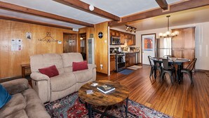 Ein gemütliches Wohnzimmer mit einer Couch, einem Couchtisch, Holzböden und einer Küche mit modernen Geräten.