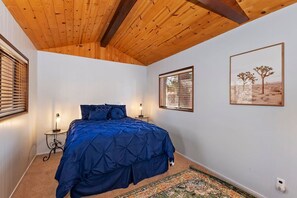 Un dormitorio con una cama, dos mesitas de noche, techo de madera y un cuadro enmarcado en la pared.