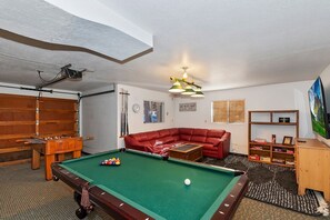 Una mesa de billar con un sofá rojo y una estantería en una habitación con paredes blancas y techo inclinado.