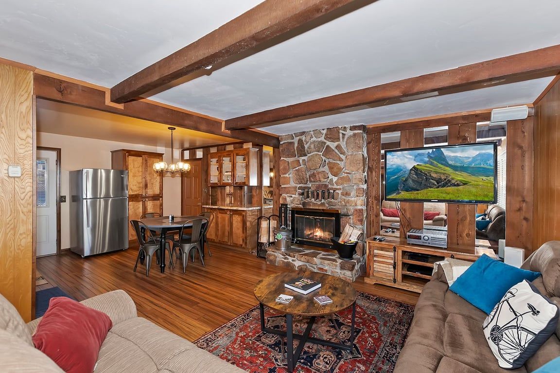 A cozy living area with a stone fireplace, a television, and a dining space with a refrigerator.