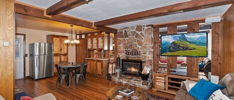 A cozy living area with a stone fireplace, a television, and a dining space with a refrigerator.