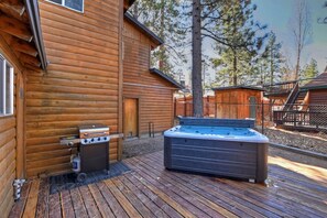 Una cabaña de madera con jacuzzi y parrilla en el exterior.