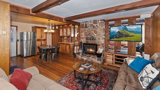 Ein gemütliches Wohnzimmer mit Kamin aus Stein, Holzbalken, einem großen Fernseher und einem Essbereich.