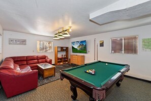Una sala con piscina que incluye mesa de billar, sofá de cuero rojo y estantería.