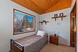 A bedroom with a bed, a nightstand, a window with blinds, and a door.