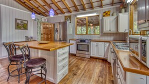 A kitchen with wooden beams, white cabinets, a central island with bar stools, stainless steel appliances, and a window with a view. - Apartment by the Caribbean sea. 4 min walk from the beach! Air-conditioning! (Limón Province)