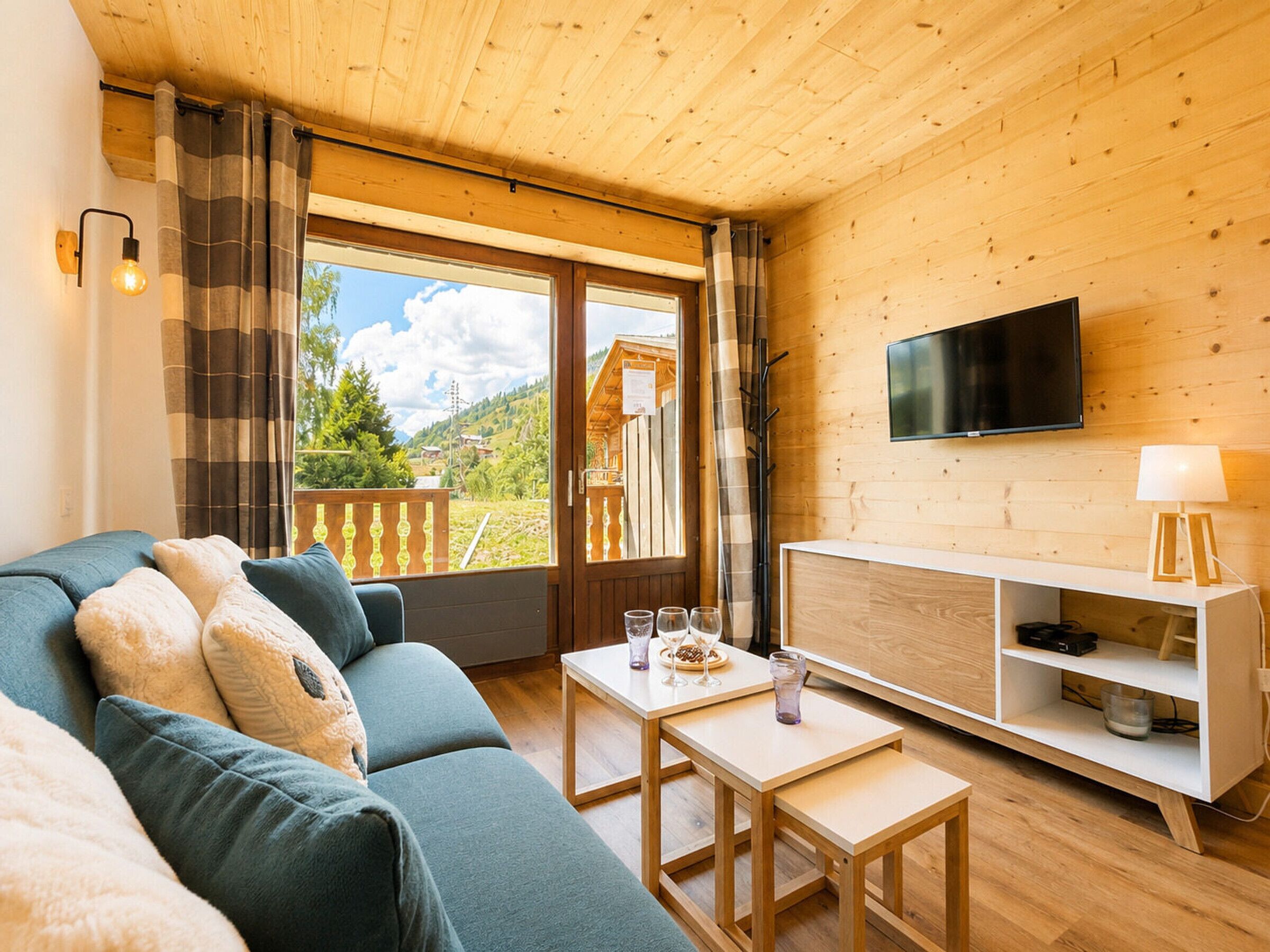 A cozy living room with a sofa, a TV mounted on the wall, and a balcony with a wooden fence.