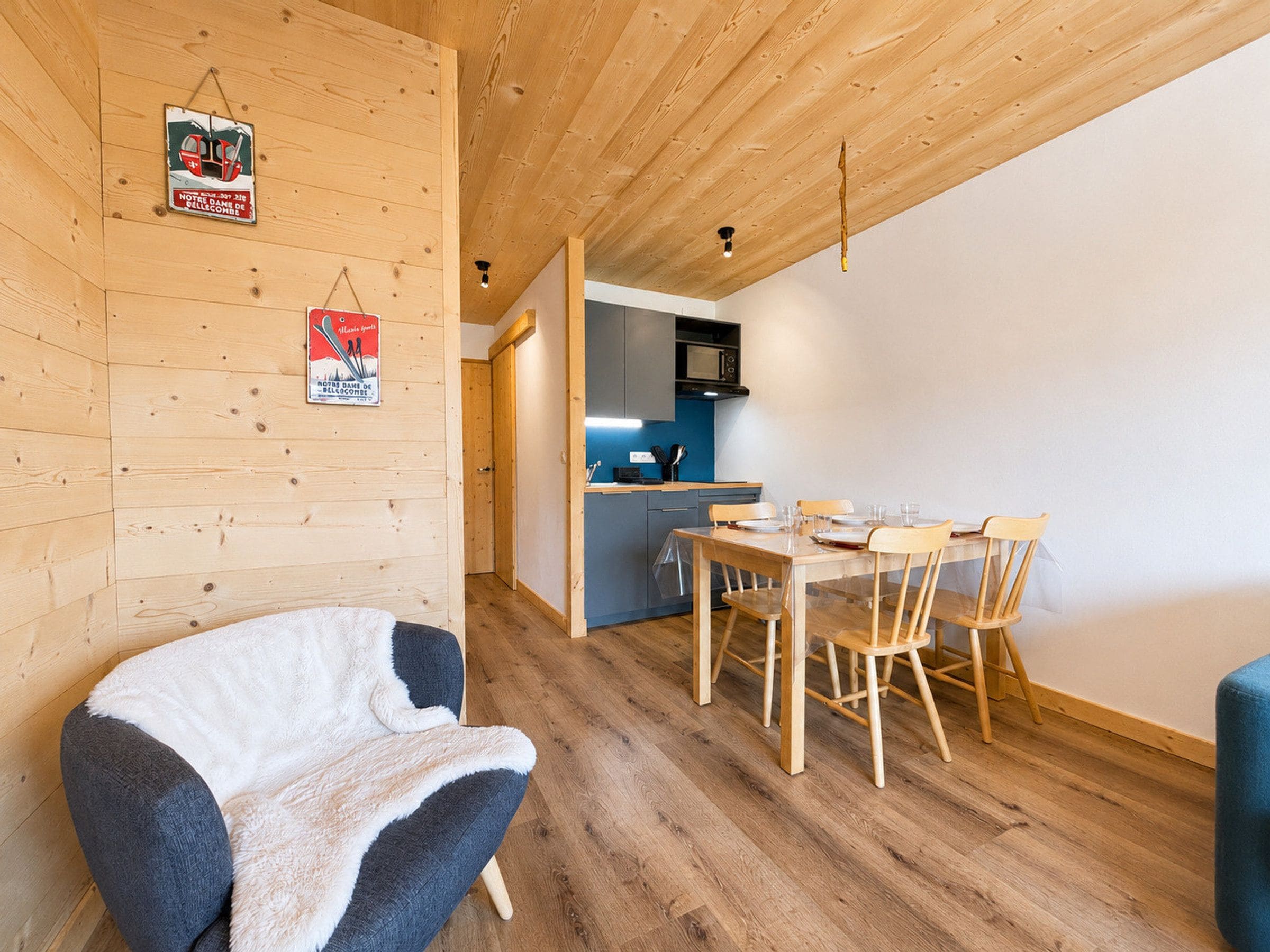 A cozy room with a wooden ceiling, a dining table with chairs, and a kitchen area with a microwave.