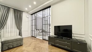 A modern living room with a wooden floor, a grey sofa, a black entertainment unit, and a sliding glass door leading to a balcony. - Home Apart Sverdlova str 26 (Minsk)