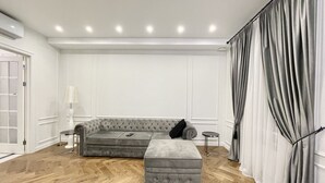 A modern living room with a grey sectional sofa, a grey ottoman, a small side table, and a lamp. - Home Apart Sverdlova str 26 (Minsk)