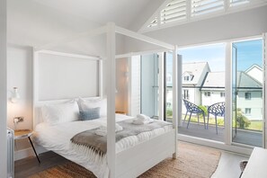 A bedroom with a four-poster bed, a bedside table, a lamp, and a view of the outside.