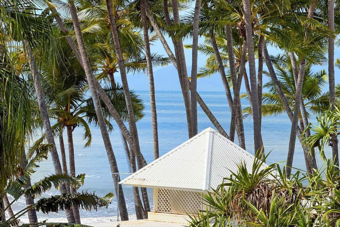 A beach view with palm trees and a white building with a triangular roof.