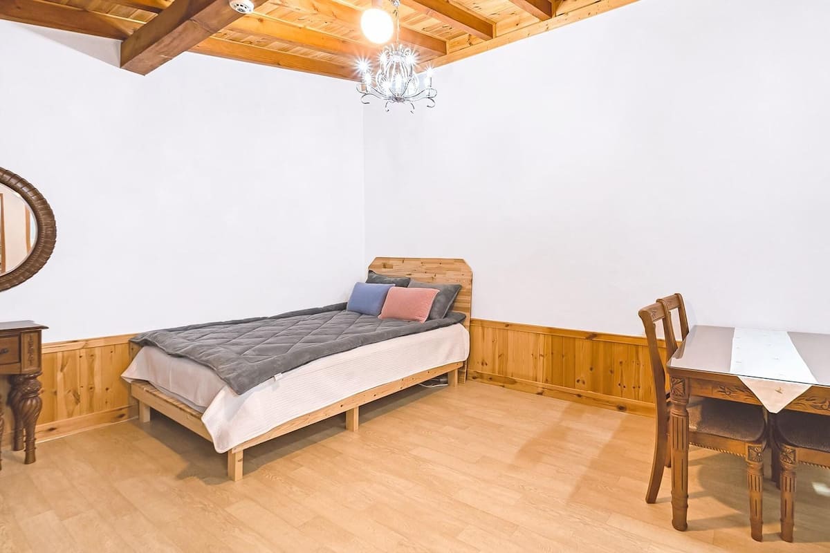 Ein Schlafzimmer mit einem hölzernen Bett, einem Tisch, Stühlen, einer Chandelier und einem Spiegel.