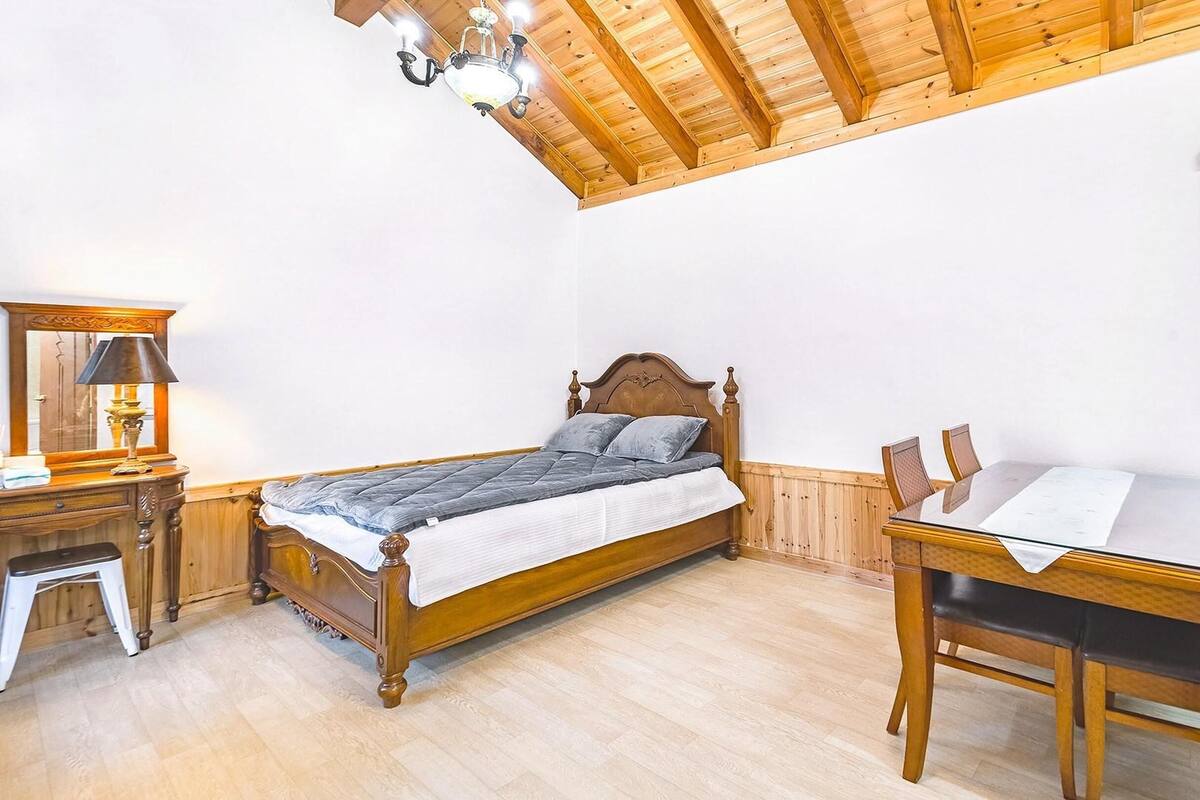 Ein Schlafzimmer mit einem hölzernen Bett, einem kleinen Nachttisch, einem Spiegel und einem Esstisch mit Stühlen.