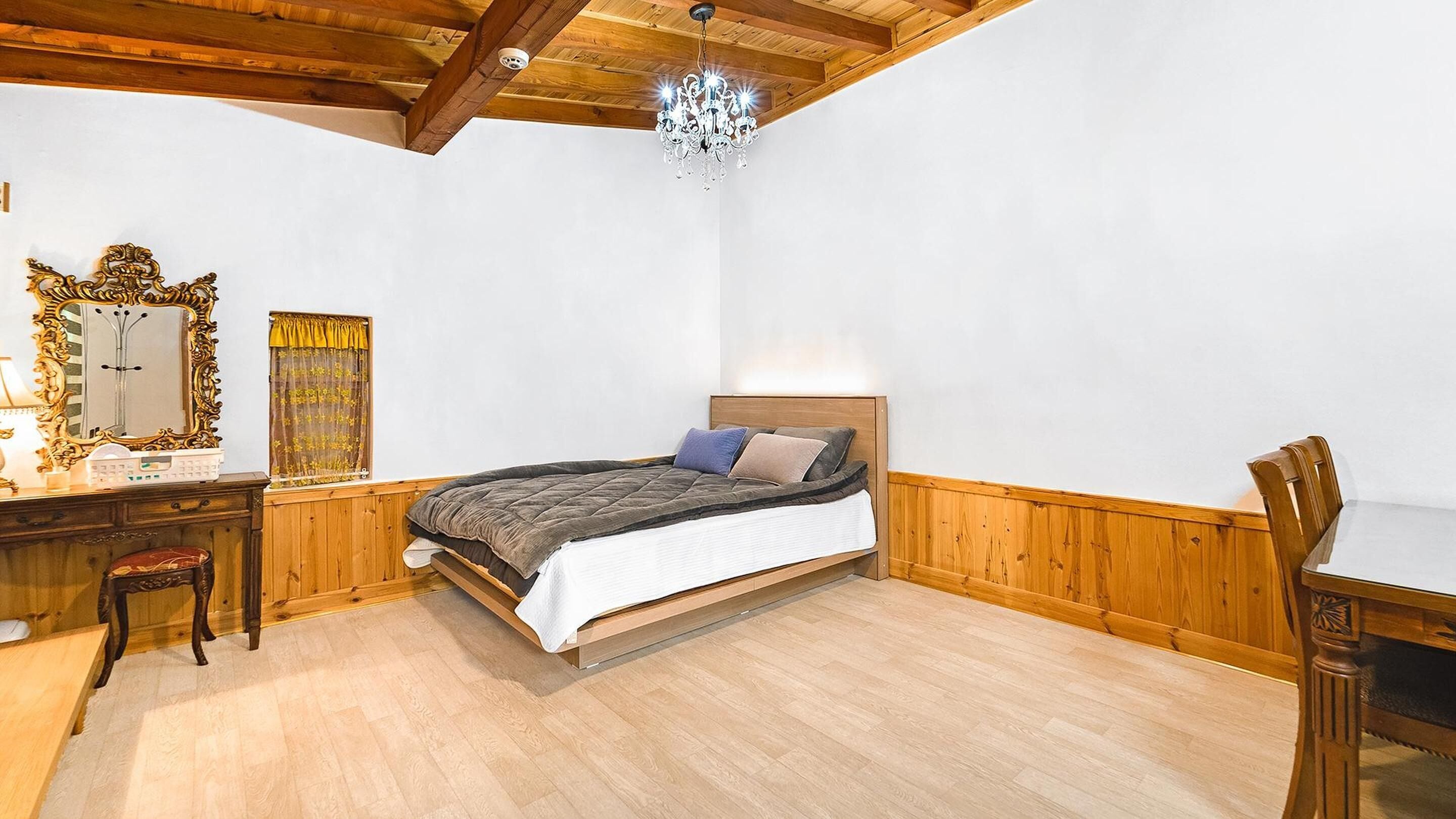 Un dormitorio con techo de madera, una cama con colcha acolchada, una mesita de noche, una silla, un espejo y una araña.