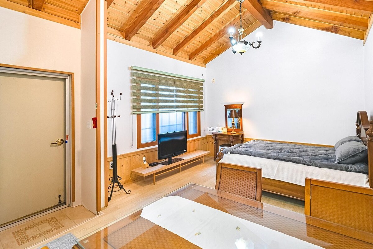 A bedroom with a bed, a television, a desk, and a window with blinds.