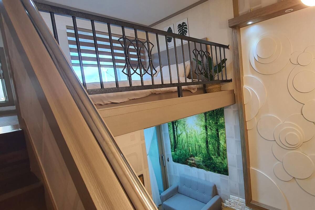 Une chambre avec un lit superposé, une fenêtre donnant sur la forêt et un mur décoratif orné de motifs circulaires.