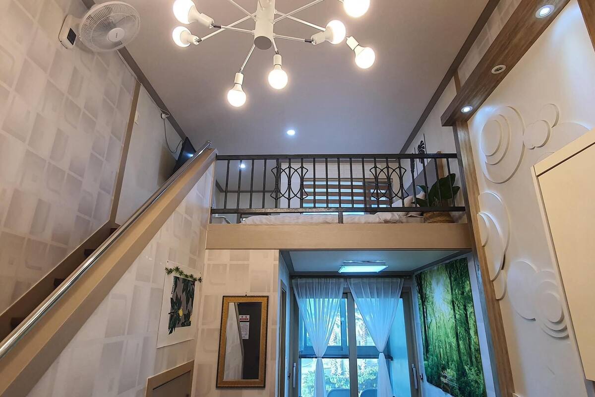 Un escalier avec une rampe en métal menant à un balcon, un ventilateur de plafond et un luminaire moderne.