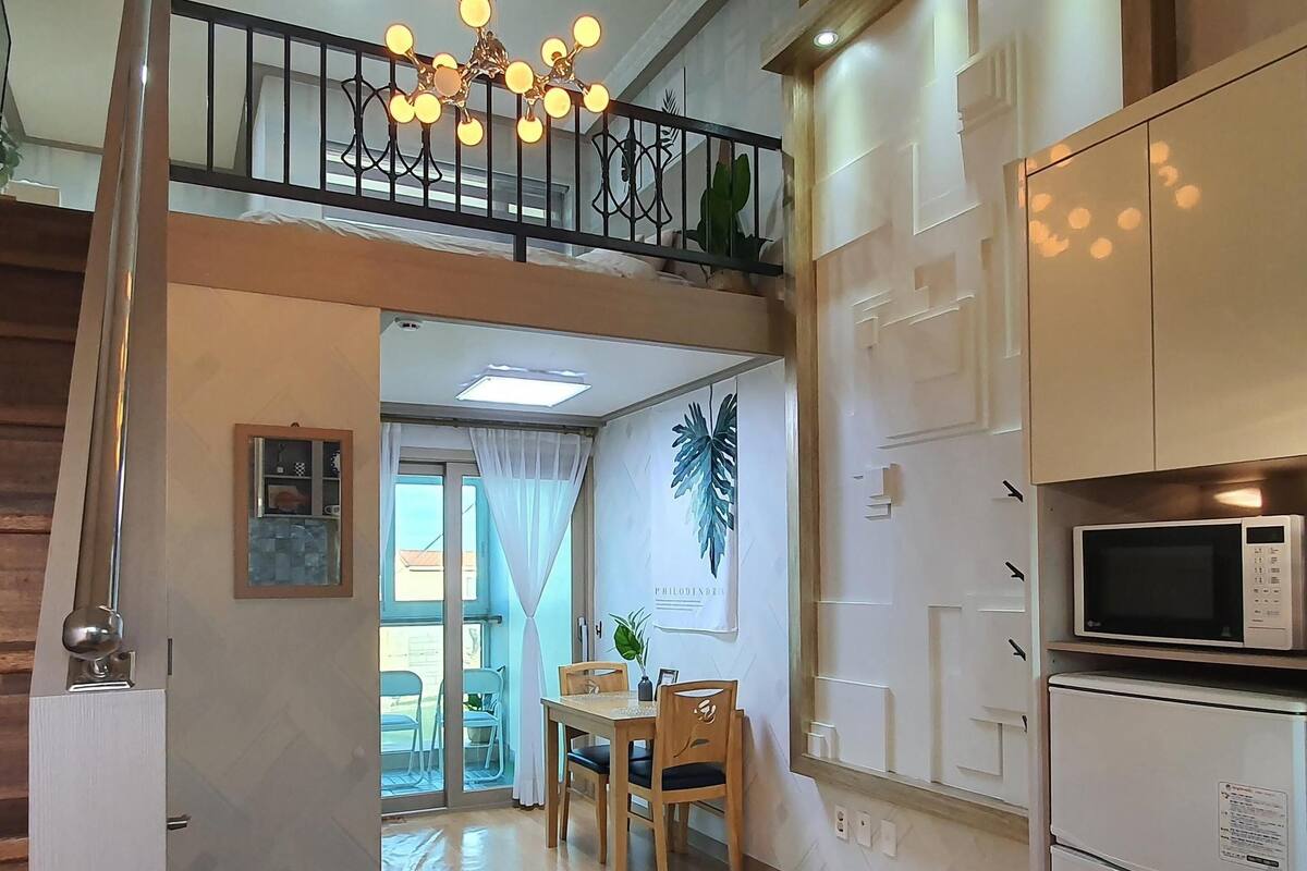 Une cuisine moderne équipée d’un four à micro-ondes et d’un réfrigérateur, un coin repas avec une table et des chaises, et un escalier menant à un niveau supérieur.