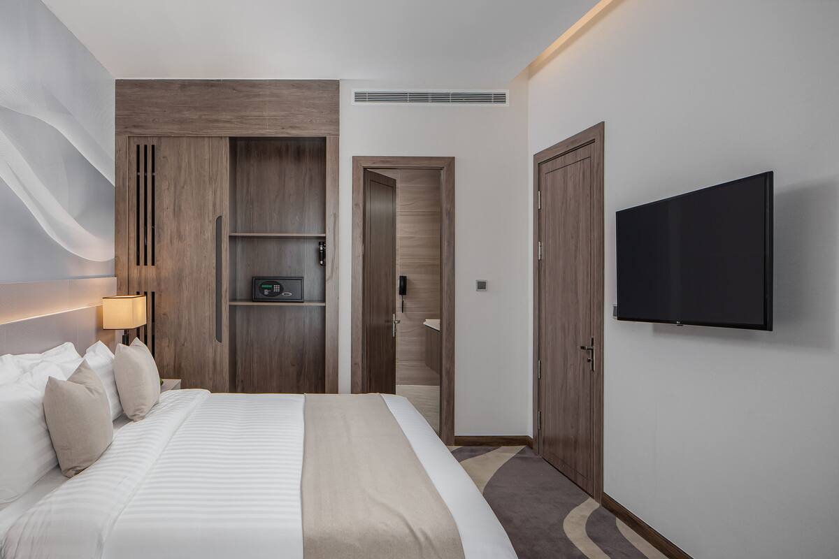 Una camera d'albergo con un letto grande, una TV a parete e un armadio in legno.