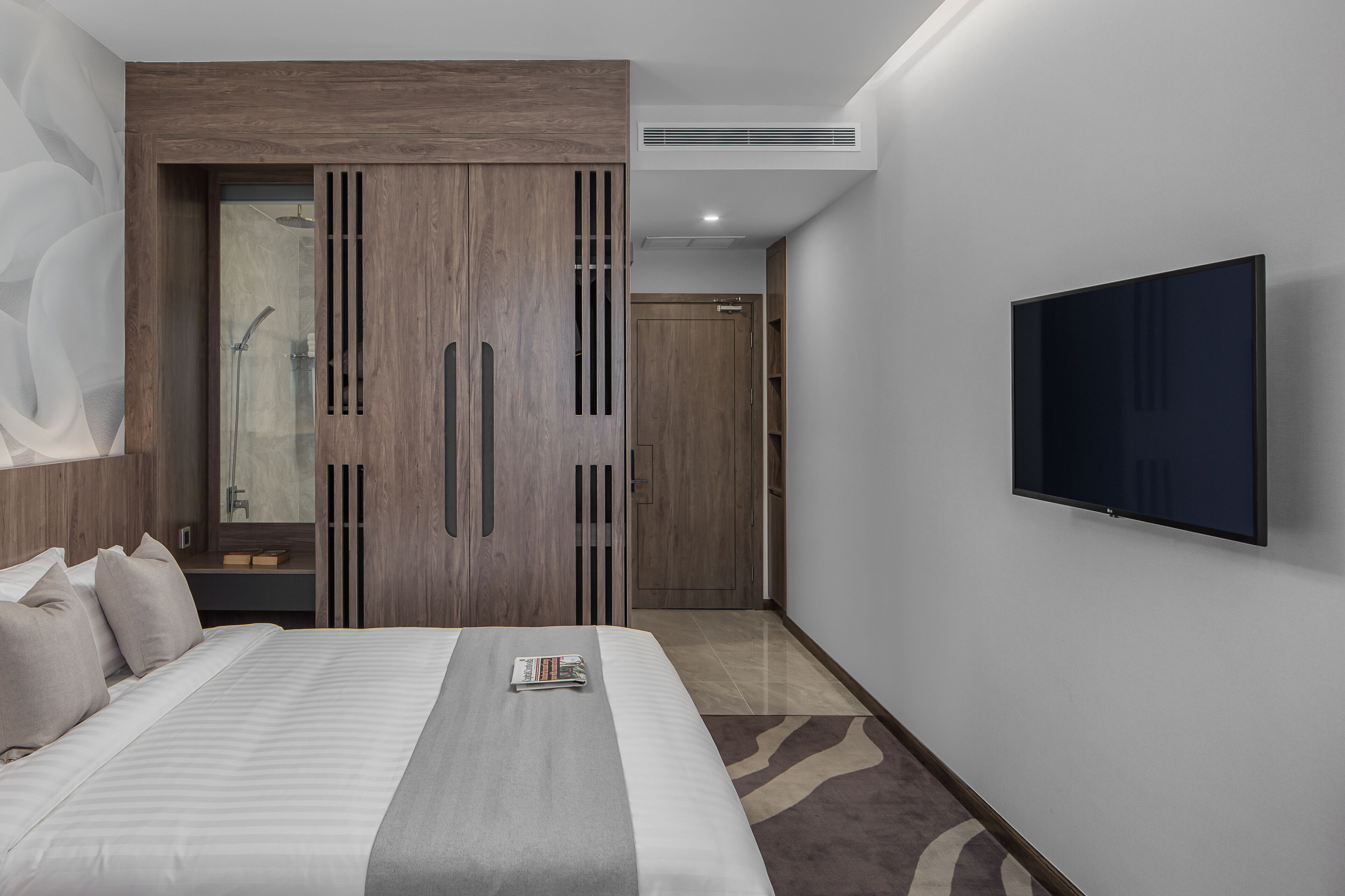 Una habitación de hotel moderna con una cama grande, un televisor de pantalla plana, un armario de madera y zona de ducha.