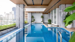 A modern indoor swimming pool with clear blue tiles, wooden ceiling, and potted plants.